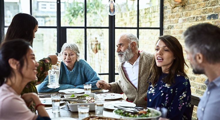 Extended family sitting round dinner table chatting and eating dinner